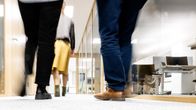 Feet and legs of three people in a bright office hallway.