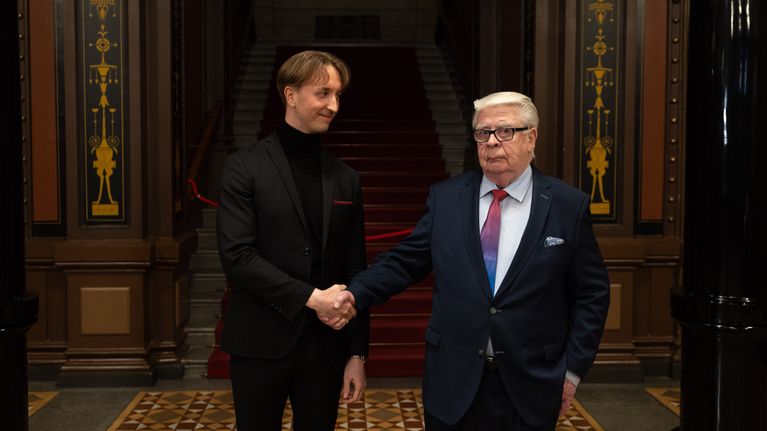 Kalervo Kummola ja Ilmari Nurminen kättelevät. Kummola katsoo kameraan.