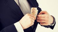 Man in dark suit, white shirt and polka-dotted necktie putting a couple of 50-euro bills in his jacket pocket.