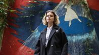 Darja Heikinen katsoo kameraan, taustalla puna-sini-valkoinen muraali, jossa balleriina