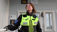 Nainen tummassa virka-asussa ja keltaisessa huomioliivissä, taustalla tullin kyltit suomeksi ja norjaksi.