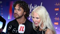 Woman and man speaking into reporters' microphones with a purple screen in the background.