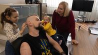 Miehen tyttäret koskettavat isän päätä, isä hymyilee. Äiti katsoo lapsia ja hymyilee.