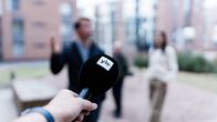 Yle microphone in the foreground of the image, interviewees outdoors in the background.