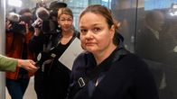 Woman in dark sweater looking into the camera, with a group of photographers and reporters seen in the background.