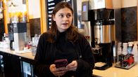 En person i svarta kläder står vid en kafédisk och håller i en mobiltelefon.