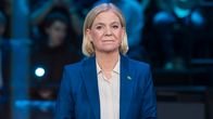 Magdalena Andersson i en vit skjorta och blå kavaj står vid ett talarpodium och tittar framåt. På podiet står två glas.
