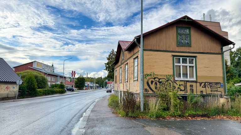 Vanha keltasävyinen puutalo, jonka seinissä on erivärisiä graffiteja. Vieressä Pispalan valtatie.