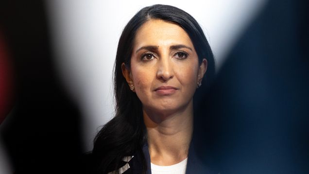 Nasima Razmyar i en svart kavaj och vit blus tittar framåt. I bakgrunden syns en vit vägg.