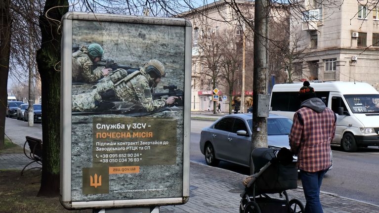 En man med en barnvagn går förbi en rekryteringsaffisch för ukrainska soldater i Zaporizjzja.