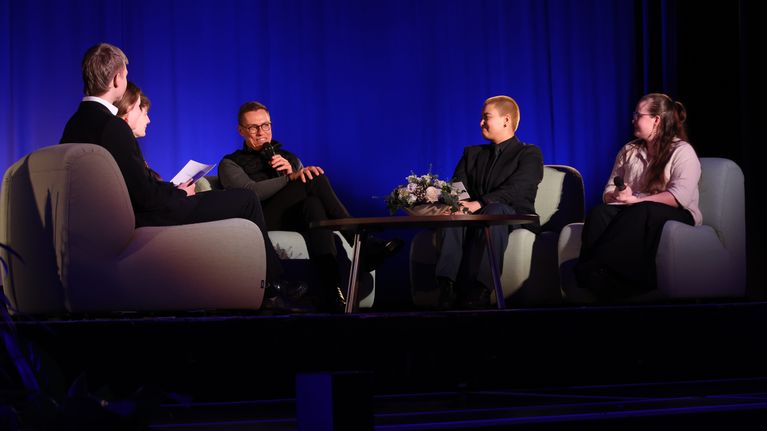 Presidentti Alexander Stubb situu pöydän ääressä lavalla ja muilla penkeillä on nuoren näköisiä henkilöitä.