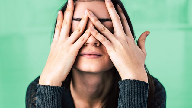 A sad-looking woman covers her face with her hands.