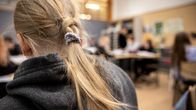 Pitkä tukkainen tyttö etualalla täydessä luokkahuoneessa.