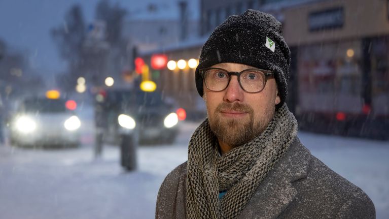 Mies katsoo lumituiskeessa hymyillen kameraan.