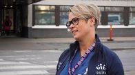 Ljushårig kvinna med glasögon står framför ingången till ett sjukhus.