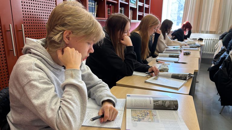 Oppilaita luokkahuoneessa kirjojen ja vihkojen kanssa.