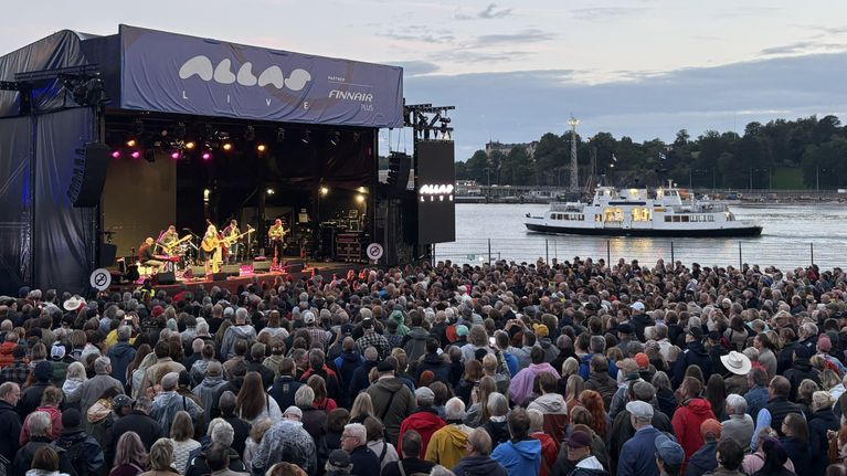Band på scen inför publik vid salutorget i Helsingfors. I bakgrunden åker en färja. 