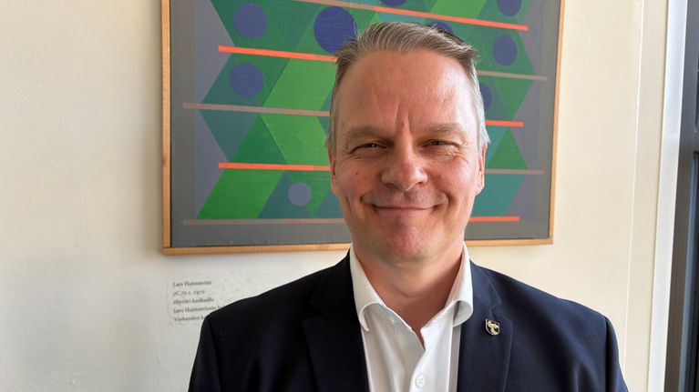 Varkauden kaupunginvaltuuston puheenjohtaja Timo Suhonen (sd.) seisoo taulun edessä.