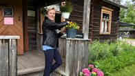 Kunnanjohtaja Eija Liikamaa seisoo portailla ja asettelee kukkia ruukkuun Huovilanpuiston kahvilarakennukssen sisäänkäynnin kaiteella.