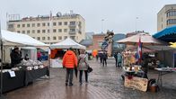 Torilla kojuja, ilmapallojen myyjä ja ihmisiä kävelemässä.