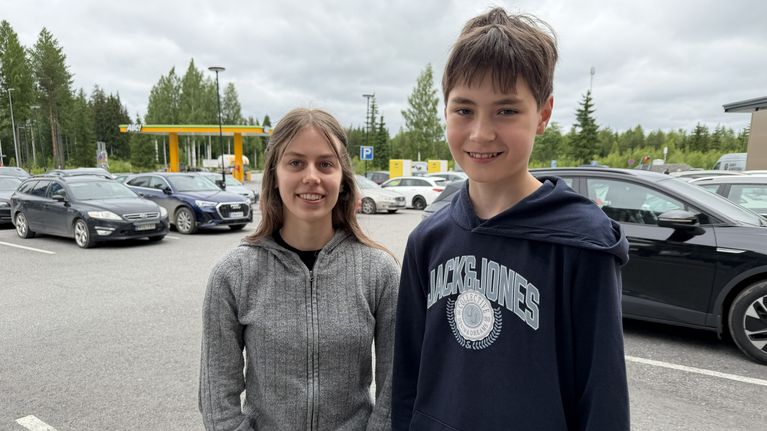 Tyttö ja poika seisovat parkkipaikalla.