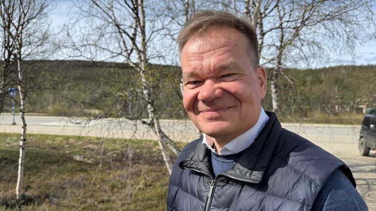 Veli-Matti Ruotsalainen katsoo suoraan kameraan ja hymyilee taustanaan tie ja maisemat.