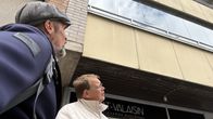 Kaksi henkilöä seisovat kadulla ja katselevat viereisen talon julkisivua.