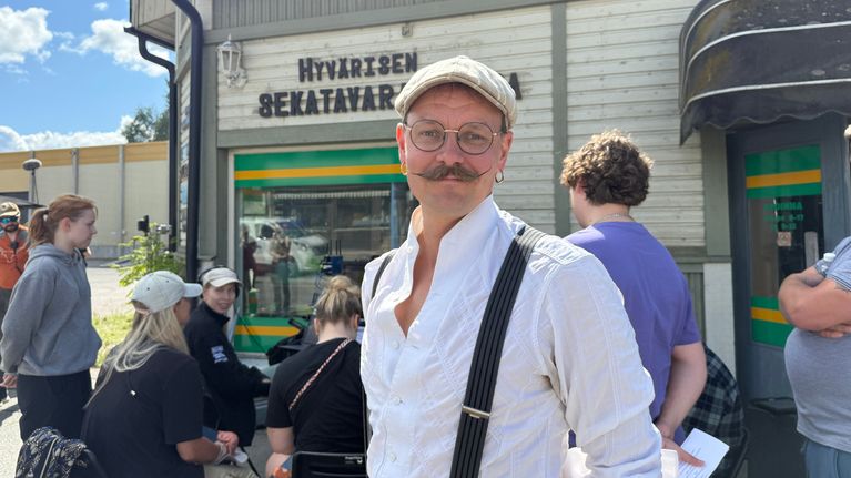  Ylä-Savon kerma -sarjan tuottaja Antti Kairakari katsoo hymyillen kameraan. Taustalla näkyy kuvausryhmää.