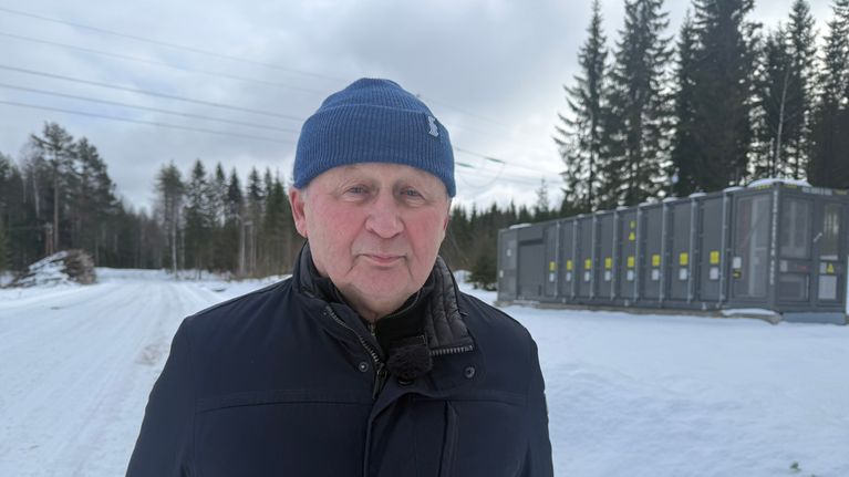 Järvi-Suomen Energian hallituksen puheenjohtaja Jaakko Hänninen seisoo uuden akkuvaraston edustalla. Taustalla näkyy Fingridin voimalinja.