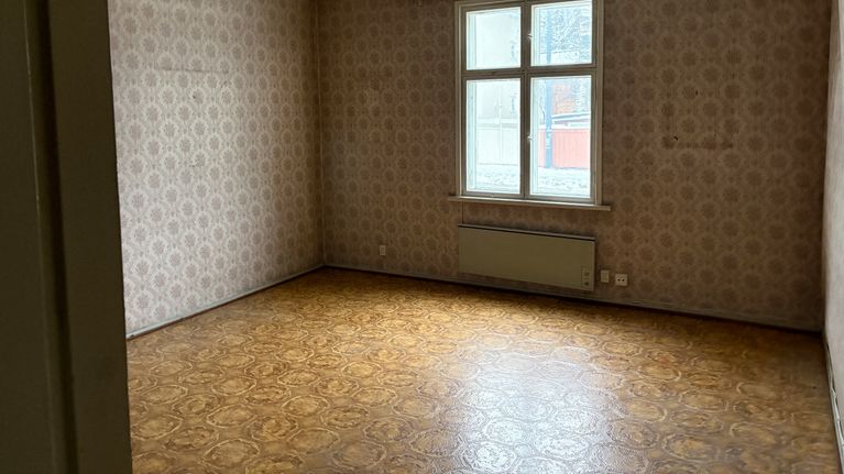 Kuvassa näkyhy vanha tyhjä huone, kuviollisine tapetteineen ja lattioineen. Peräseinässä ikkuna ulos.