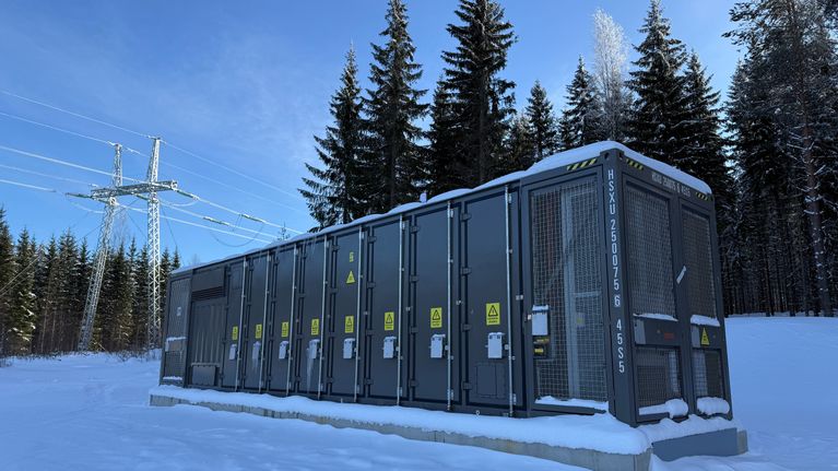 Kuvan etualalla 1,25 megawatin akkuvarastolla ja taustalla näkyy Fingridin voimalinja.