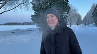 Pipopäinen nainen lumisessa maisemassa. Taustalla näkyy kevyen liikenteen väylä ja jäätynyt joki.