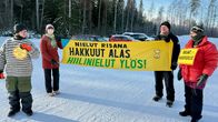 Neljä henkilöä mielenosoituskylttien kanssa talvisella parkkipaikalla. Lakanassa lukee: Nielut risana, hakkuut alas, hiilinielut ylös.