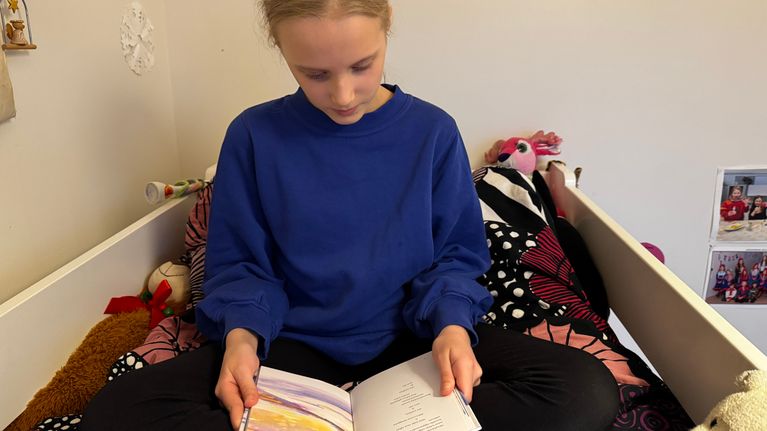 Elle-Maija Niittyvuopio-Jämsä lukee saamenkielistä runokirjaa sängyssään yläpetillä.