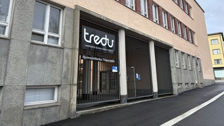 A building on a city street, with a sign at a gate that reads "Tredu", and other text that is too small to read easily.