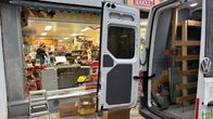 Etnisen ruokakaupan rikkinäisen ikkunan edessä seisoo pakettiauto ja kadulle on tuotu tavaraa.