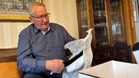 Mies avaa uutta ylioppilaslakkia kotinsa olohuoneessa.