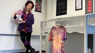 Kuvassa henkilö seisoo sisätiloissa pitäen kädessään taideteosta. Taustalla on seinälle kiinnitetty liitutaulu.