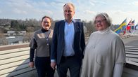 Två kvinnor och en man står på en balkong. I bakgrunden syns centrum av en småstad.