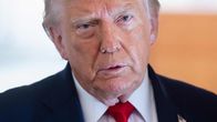 Donald Trump pukeutuneena tummaan pukuun ja punaiseen solmioon.