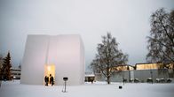 Lumesta rakennettu iso neliskanttinen kuutio, jonka keskellä on sisäänkäynti, kuution oviaukossa ihmisiä ja taustalla Rovaniemen pääkirjasto.