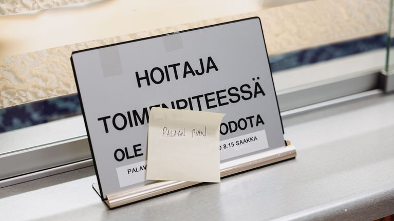 Lappu terveysaseman aulassa, jossa lukee "palaan pian".