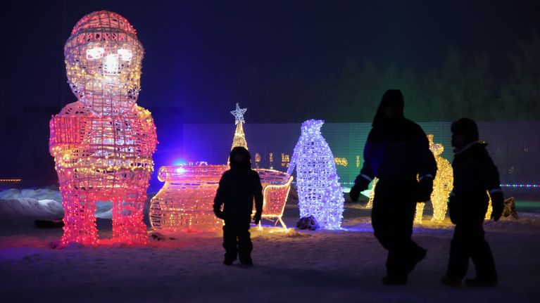 Lapsi ja kaksi aikuista talvisessa valopuistossa.