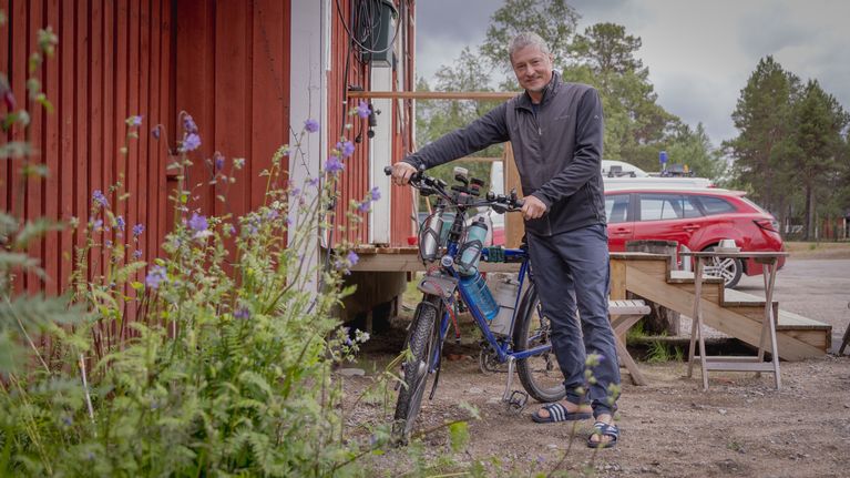 Mies hymyilee kameralle piettäessään pyörän tangosta kiinni.
