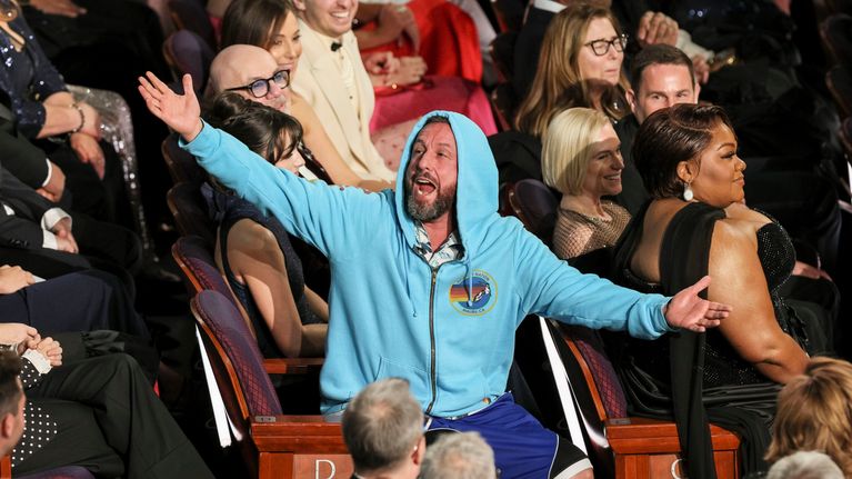 Adam Sandler vaalean sinisessä hupparissa ja shortseissa gaalan yleisössä.