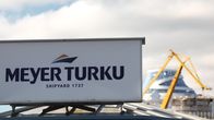 Meyer Turun telakan logo kyltissä telakan pääportilla. Taustalla näkyy telakan nosturi ja valmisteilla olevan aluksen yläosia.