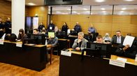 Jengirikollisia avustajineen oikeussalissa. Taustalla poliisihenkilökuntaa.