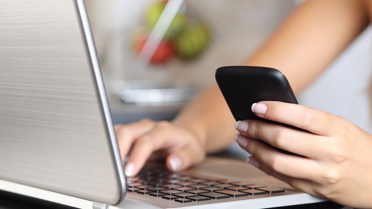 Kvinna håller i mobiltelefon och skriver på laptop