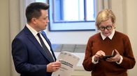 Atte Kaleva ja Paula Risikko seisovat sisätiloissa ja Atella on kädessään Kokoomuksen eduskuntaryhmän raportti maahanmuutosta.