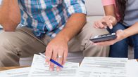 A man and a woman look at financial papers on a table with pen and calculator in hand.